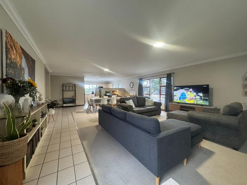 Spacious open-plan living and dining area featuring a combination of tiled and carpeted flooring, neutral wall tones, and large windows for natural light.
