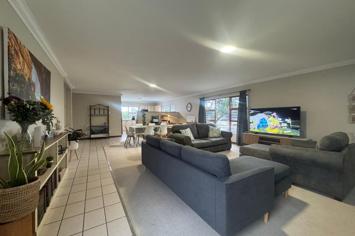 Spacious open-plan living and dining area featuring a combination of tiled and carpeted flooring, neutral wall tones, and large windows for natural light.