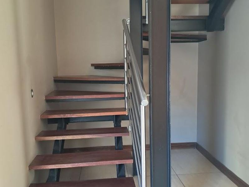 A modern open-tread staircase featuring timber steps, a robust steel frame, and a sleek stainless steel balustrade, set against neutral walls.