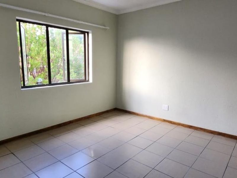 A clean, empty bedroom featuring neutral wall paint, tiled flooring, and a large window providing natural light.