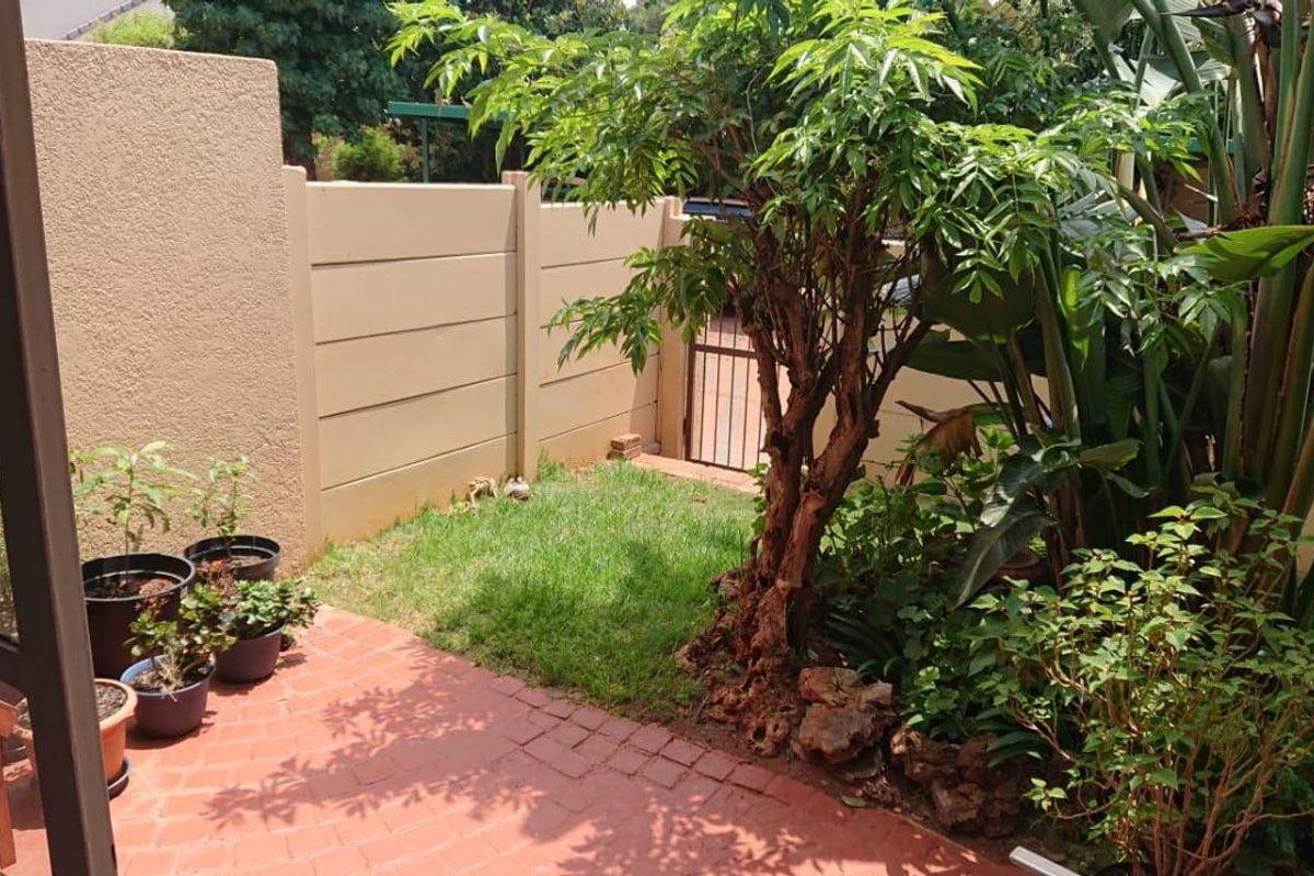 A private rear garden featuring a brick-paved patio area, established greenery, and a secure precast concrete boundary wall with a metal pedestrian gate.