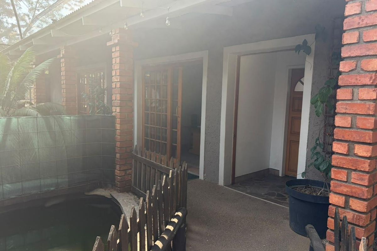 Rear exterior view of the office building featuring a covered patio, exposed brick pillars, and a small pond with a timber fence.