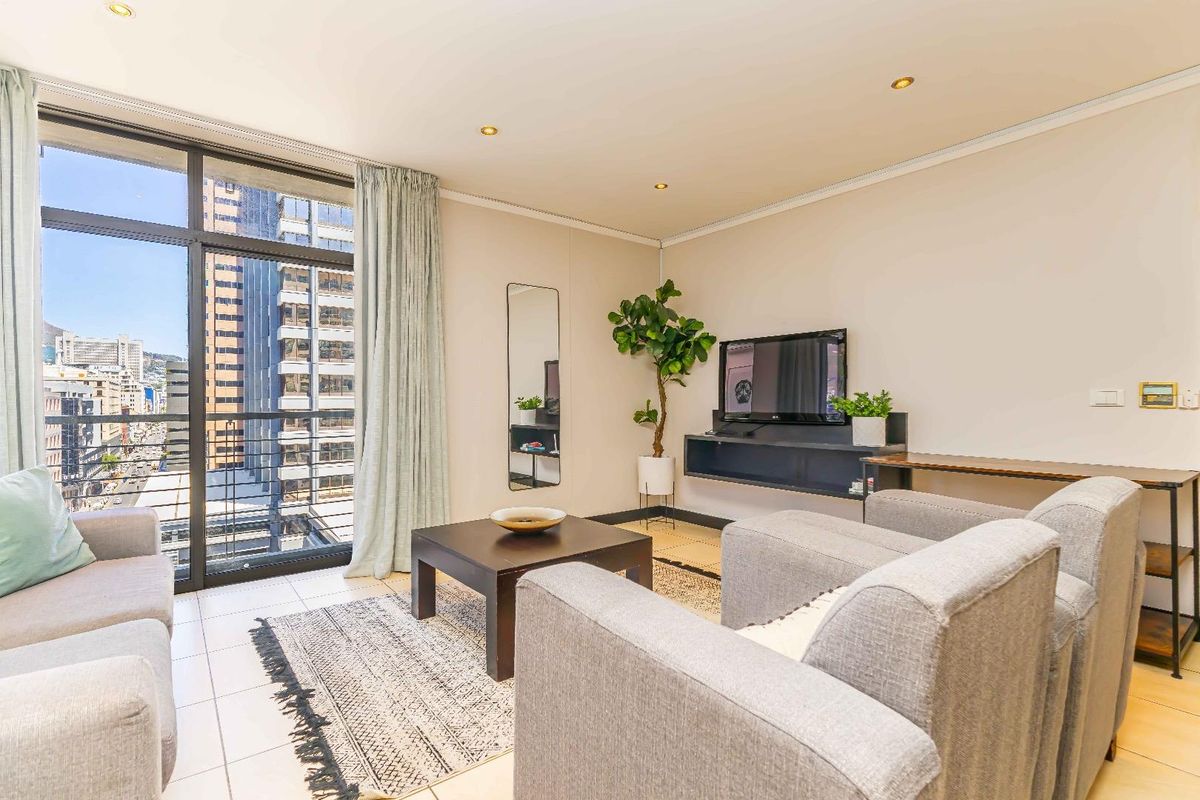A bright living room featuring tiled flooring, recessed downlights, and a large sliding glass door providing natural light and urban views.