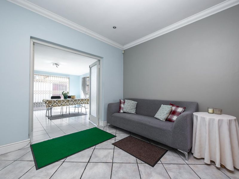 A bright living room featuring tiled flooring, crown molding, and double glass doors leading to an adjacent dining area.