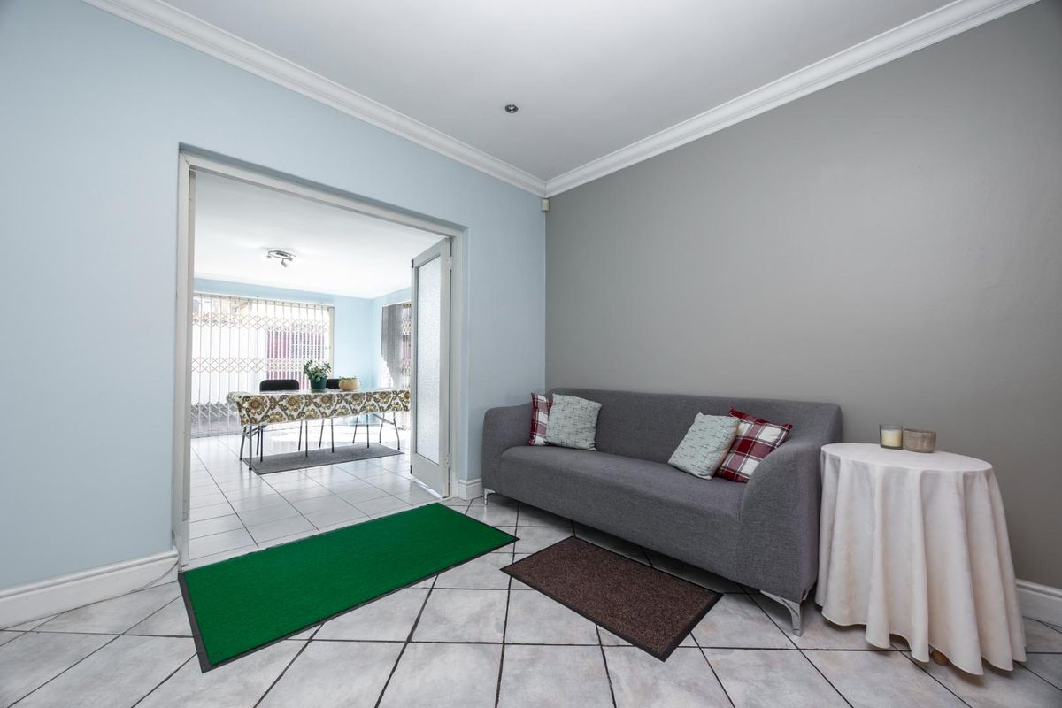A bright living room featuring tiled flooring, crown molding, and double glass doors leading to an adjacent dining area.