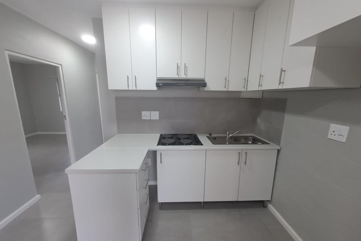 A modern, compact kitchen featuring white cabinetry, a built-in electric hob, extractor fan, and a stainless steel sink with tiled splashbacks.