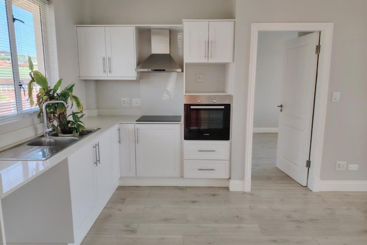 Modern kitchen featuring white cabinetry, integrated oven, electric hob, extractor fan, and light-toned laminate flooring, offering a clean and functional workspace.