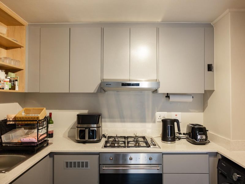 Modern kitchen featuring sleek grey cabinetry, stone countertops, a gas hob, built-in oven, and an integrated extractor fan.