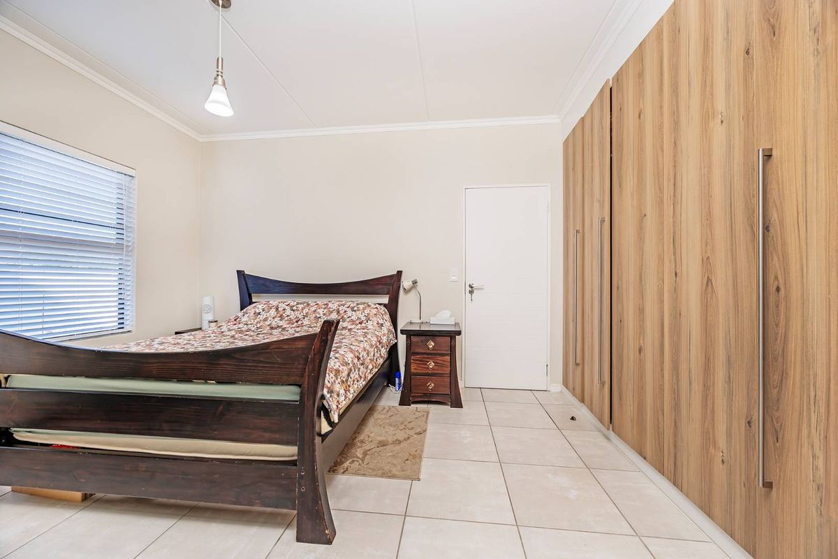 A well-lit bedroom featuring neutral tiled flooring, modern wood-finish built-in cupboards, and venetian blinds.