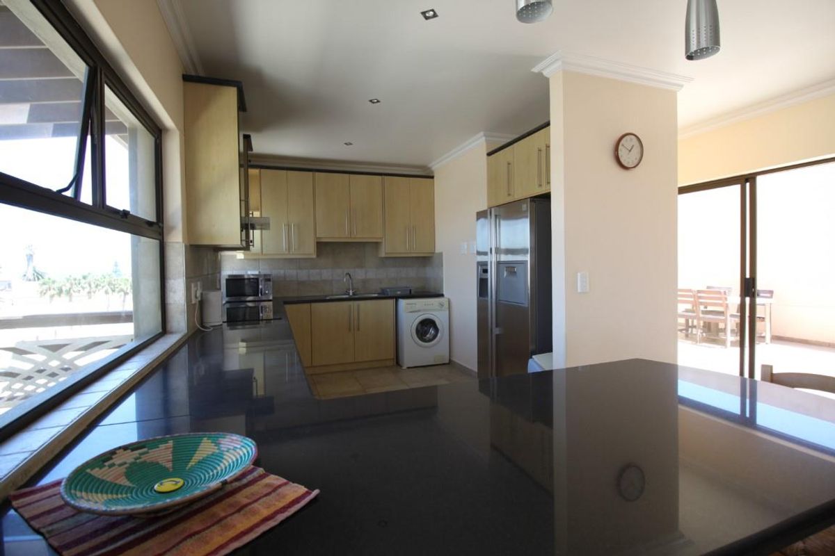A functional kitchen featuring dark granite countertops, light wood cabinetry, tiled backsplash, and integrated space for laundry appliances, opening onto a patio area.