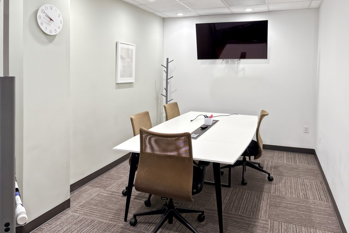 A professional office meeting room featuring carpet tiles, recessed ceiling lighting, and a wall-mounted television for presentations.