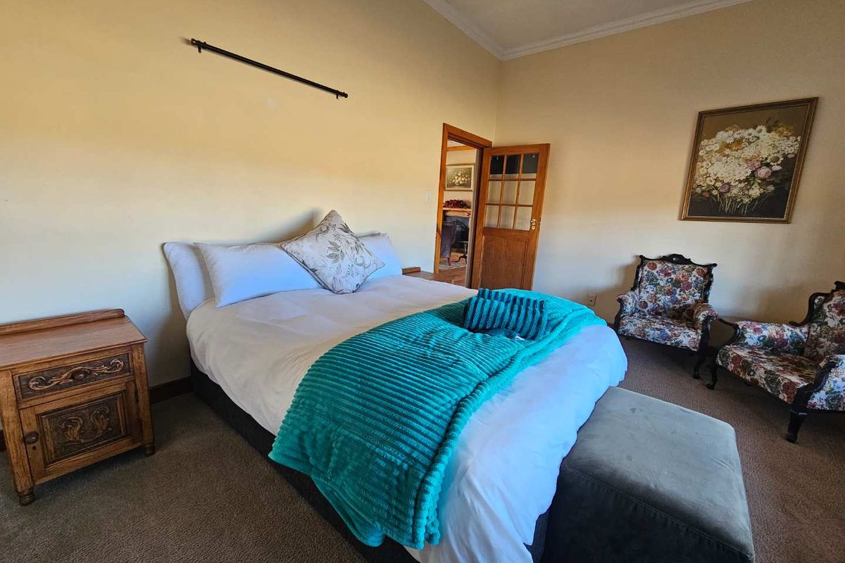 A spacious bedroom featuring neutral walls, carpeted flooring, and a classic timber door leading to an adjoining room.