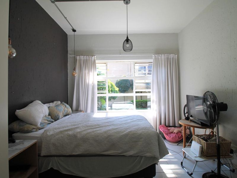 A bedroom featuring tiled flooring, a large window with natural light, and an accent wall with exposed electrical conduit and pendant lighting.