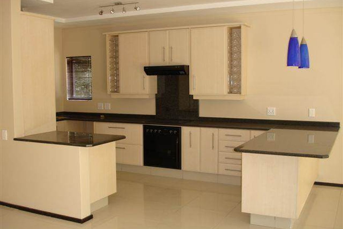 A clean, modern kitchen featuring light wood cabinetry, dark granite countertops, integrated oven, and a functional breakfast nook layout.