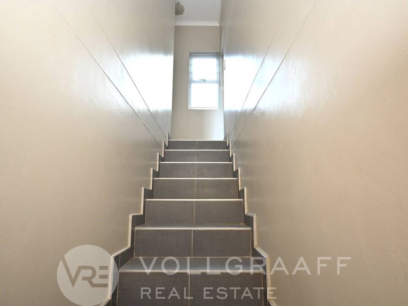 A simple, functional staircase with tiled steps leading to an upper level, featuring neutral wall finishes and a window for natural light.