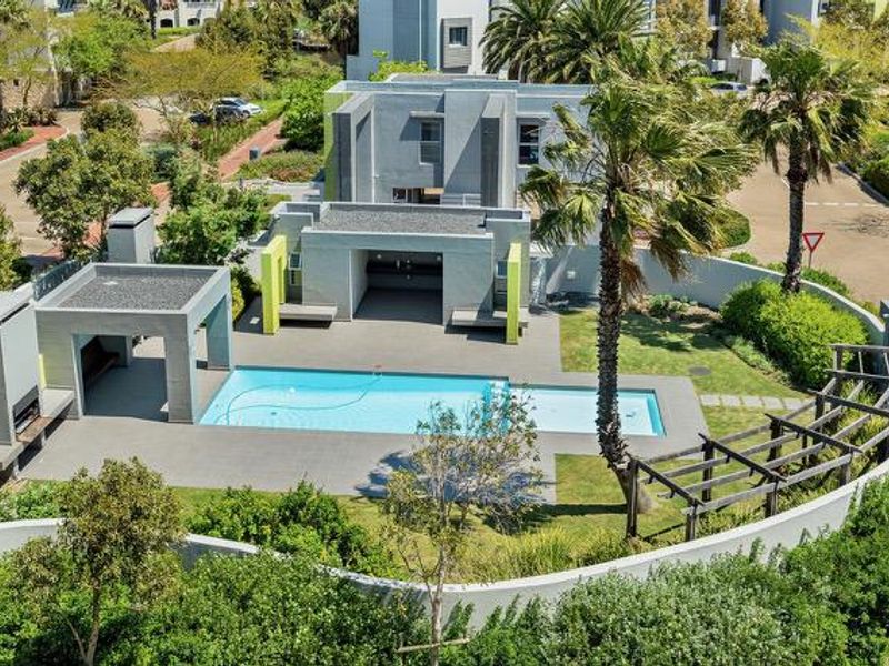 Aerial view of a communal apartment complex pool area featuring a swimming pool, built-in braai, pergola, and landscaped garden surroundings.