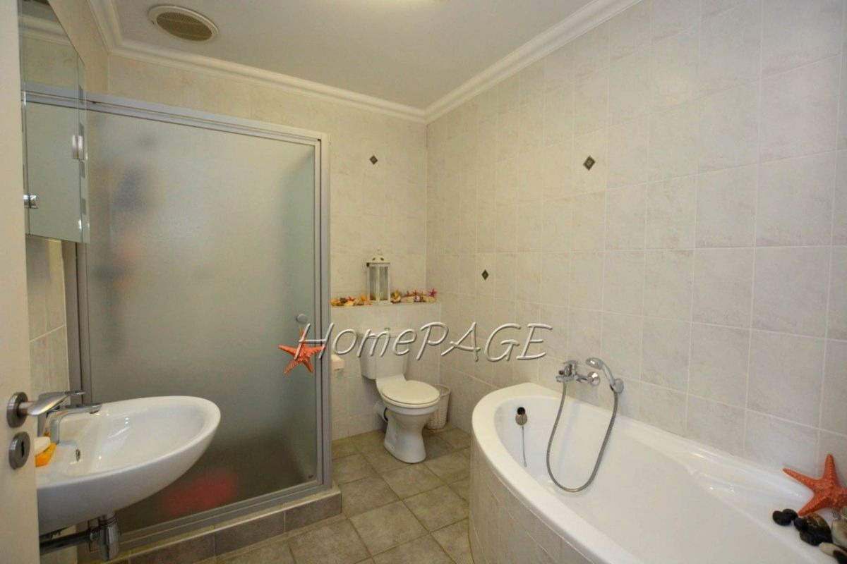 A functional bathroom featuring a corner bathtub, a separate glass-enclosed shower, a pedestal basin, and a toilet with neutral wall and floor tiling.
