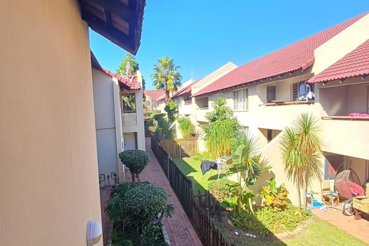 View of the apartment complex exterior featuring a brick walkway, landscaped garden areas, and residential units with tiled roofs.