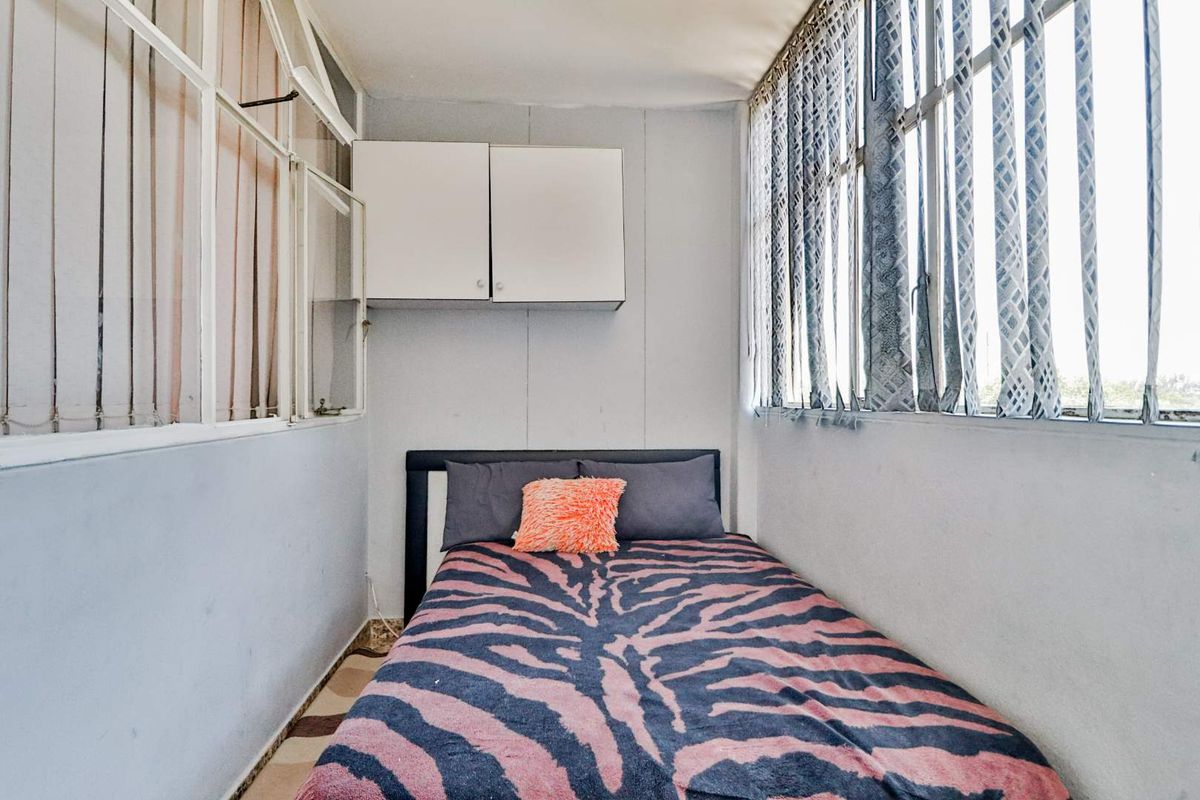 A compact bedroom featuring large windows on two sides, built-in wall cabinetry, and tiled flooring.