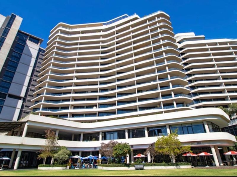 A modern high-rise apartment building featuring distinctive curved balconies, glass balustrades, and a well-maintained landscaped lawn area at the rear.
