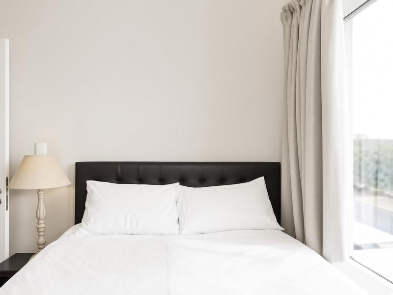 A bright and minimalist bedroom featuring a large window with neutral curtains, providing ample natural light and a clean, modern aesthetic.