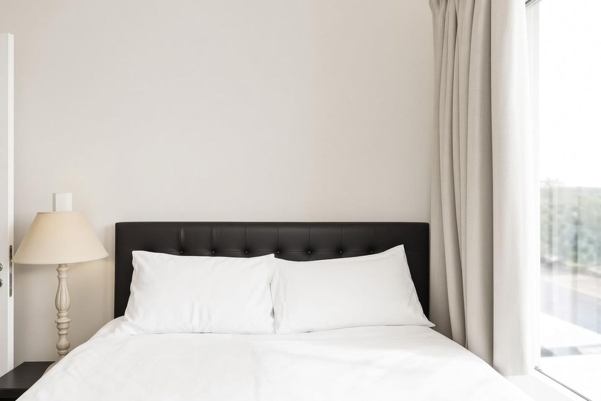 A bright and minimalist bedroom featuring a large window with neutral curtains, providing ample natural light and a clean, modern aesthetic.