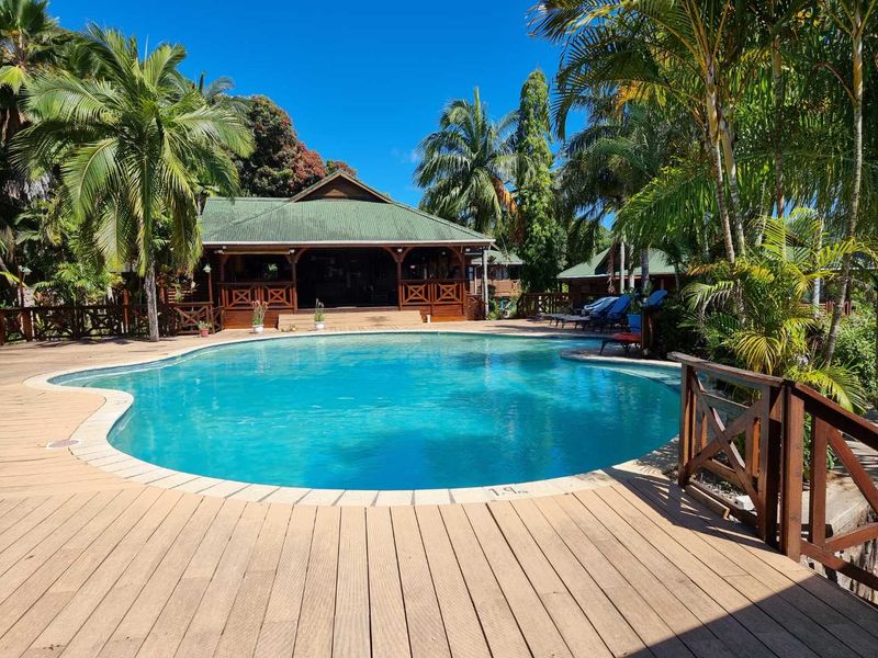 A well-maintained outdoor pool area featuring extensive timber decking, a surrounding balustrade, and a covered patio area overlooking the swimming pool.