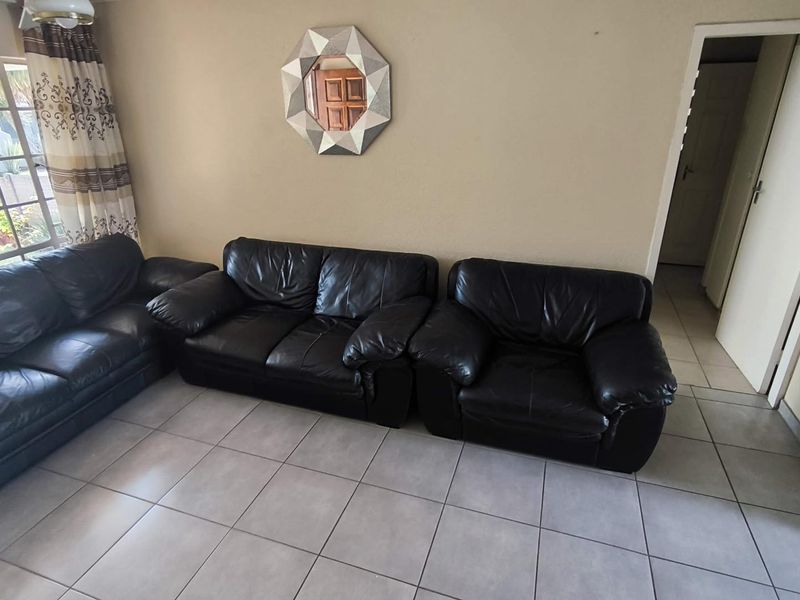 A living room area featuring neutral wall tones and tiled flooring, providing a functional space with access to adjacent rooms.