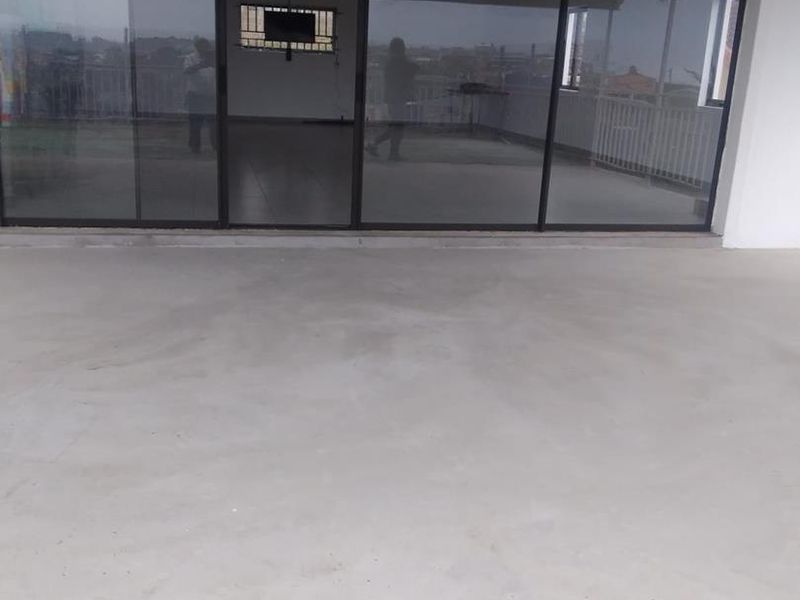 A spacious covered patio area featuring concrete flooring, large sliding glass doors, and a metal roof structure, offering a blank canvas for outdoor living.