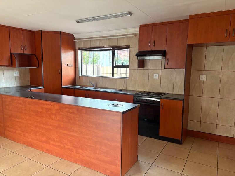 A functional kitchen featuring wood-look laminate cabinetry, tiled backsplash, a breakfast counter, and a freestanding stove with an extractor fan.