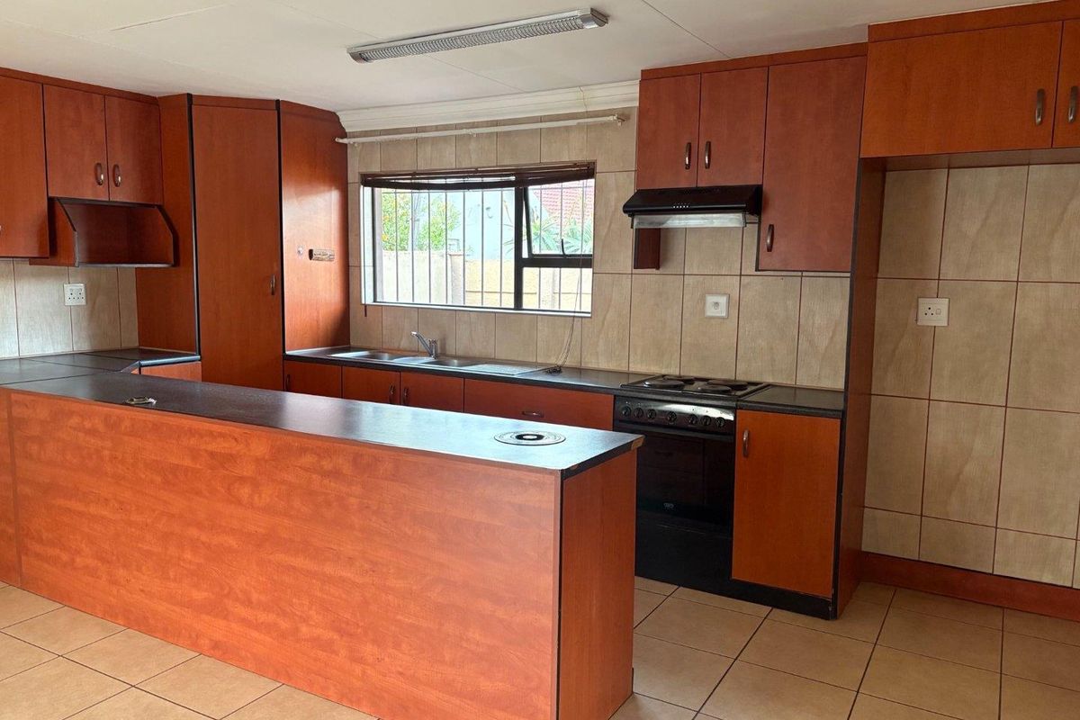 A functional kitchen featuring wood-look laminate cabinetry, tiled backsplash, a breakfast counter, and a freestanding stove with an extractor fan.