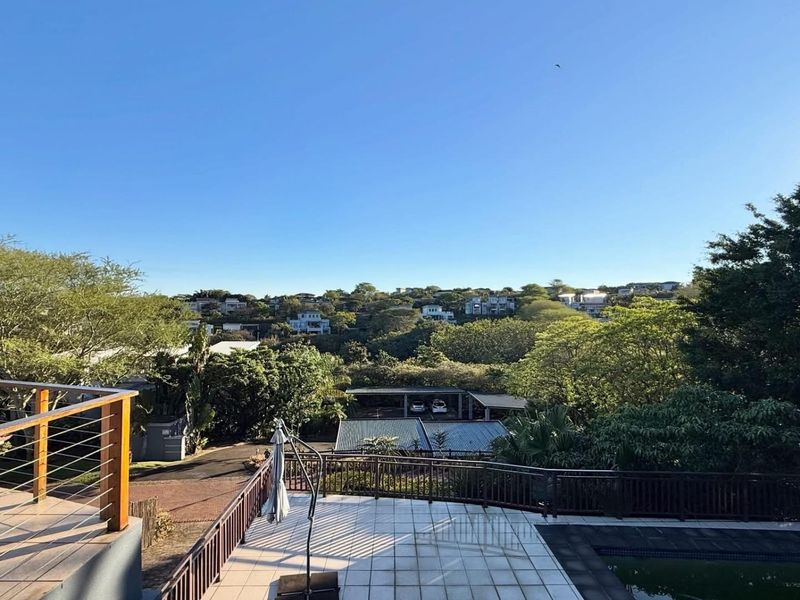 Elevated outdoor deck featuring timber balustrades, tiled patio area, and swimming pool with expansive views over the surrounding neighbourhood and lush greenery.