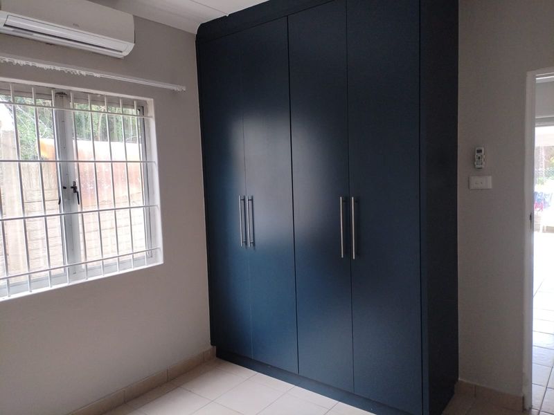 A clean bedroom featuring modern dark blue built-in cupboards, tiled flooring, and a wall-mounted split-system air conditioner.