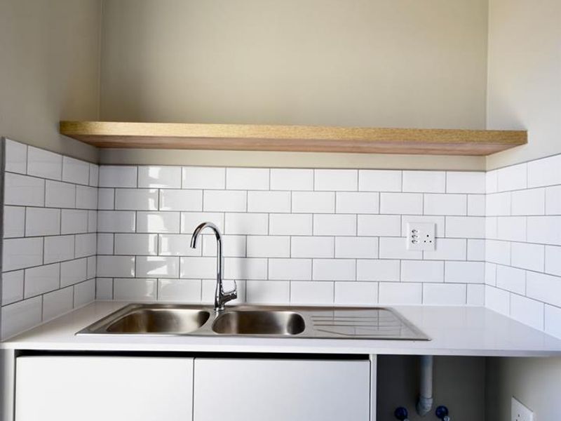 A clean and modern scullery area featuring a stainless steel double sink, subway tile backsplash, floating timber shelf, and dedicated plumbing for appliances.