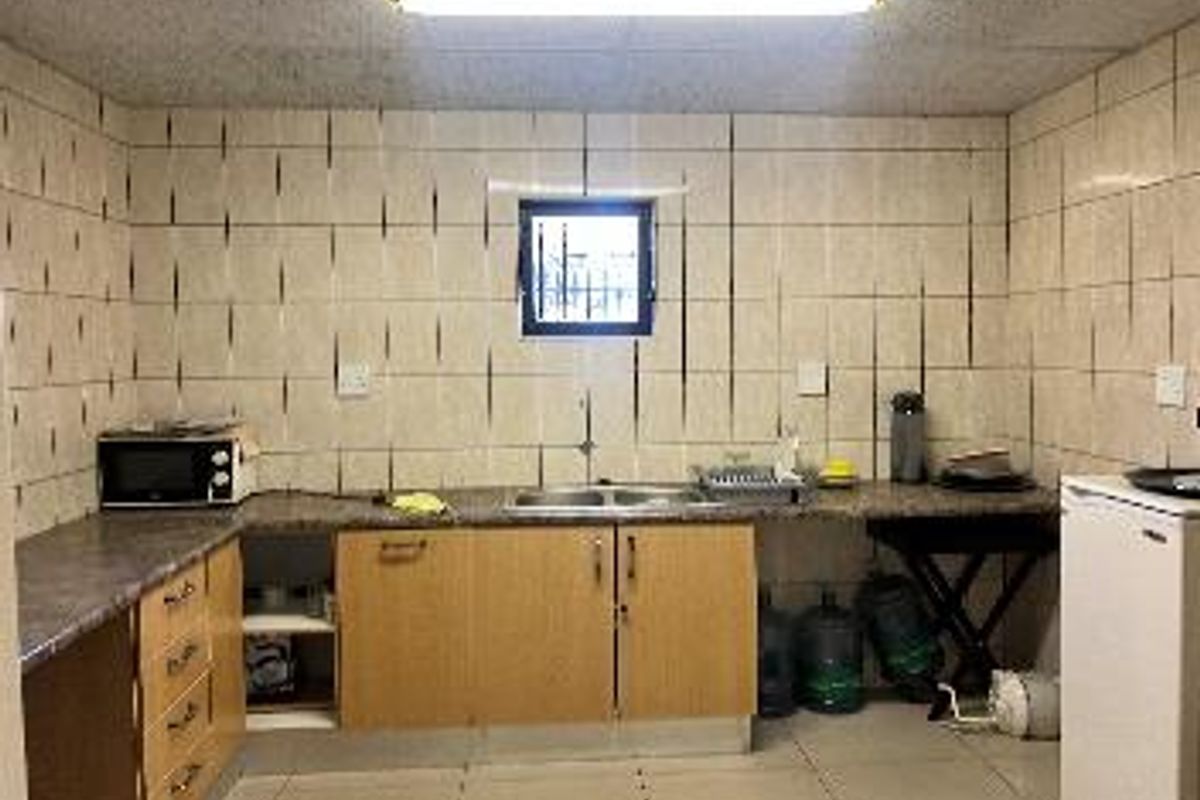 A functional industrial kitchen area featuring laminate cabinetry, a double-basin sink, and tiled wall finishes with overhead fluorescent lighting.