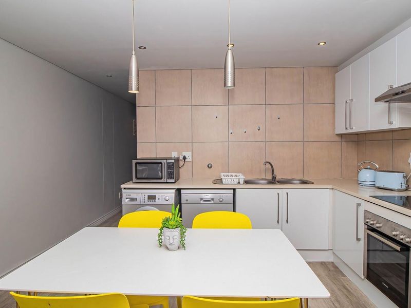 Modern open-plan kitchen featuring sleek white cabinetry, integrated appliances, a tiled splashback, and recessed lighting, seamlessly flowing into the dining area.