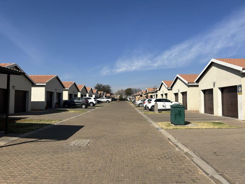 A view of the townhouse complex street featuring paved driveways, multiple garage entrances, and uniform tiled roof architecture.