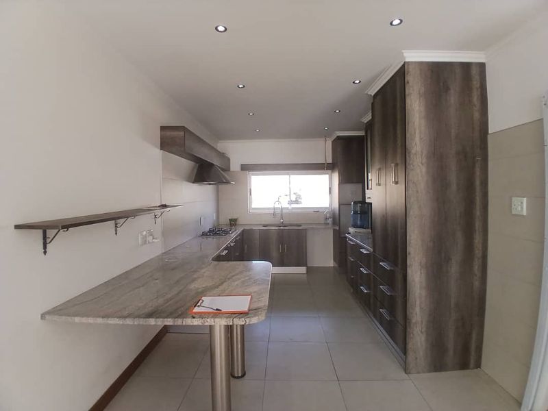 Modern kitchen featuring dark wood-grain cabinetry, stone countertops, a breakfast bar, gas hob, and recessed lighting in a clean, open layout.