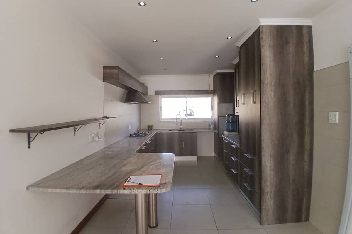Modern kitchen featuring dark wood-grain cabinetry, stone countertops, a breakfast bar, gas hob, and recessed lighting in a clean, open layout.