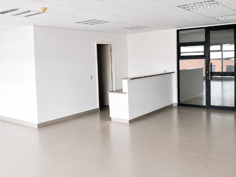 A bright, open-plan office space featuring a reception counter, tiled flooring, and a suspended ceiling with recessed lighting.