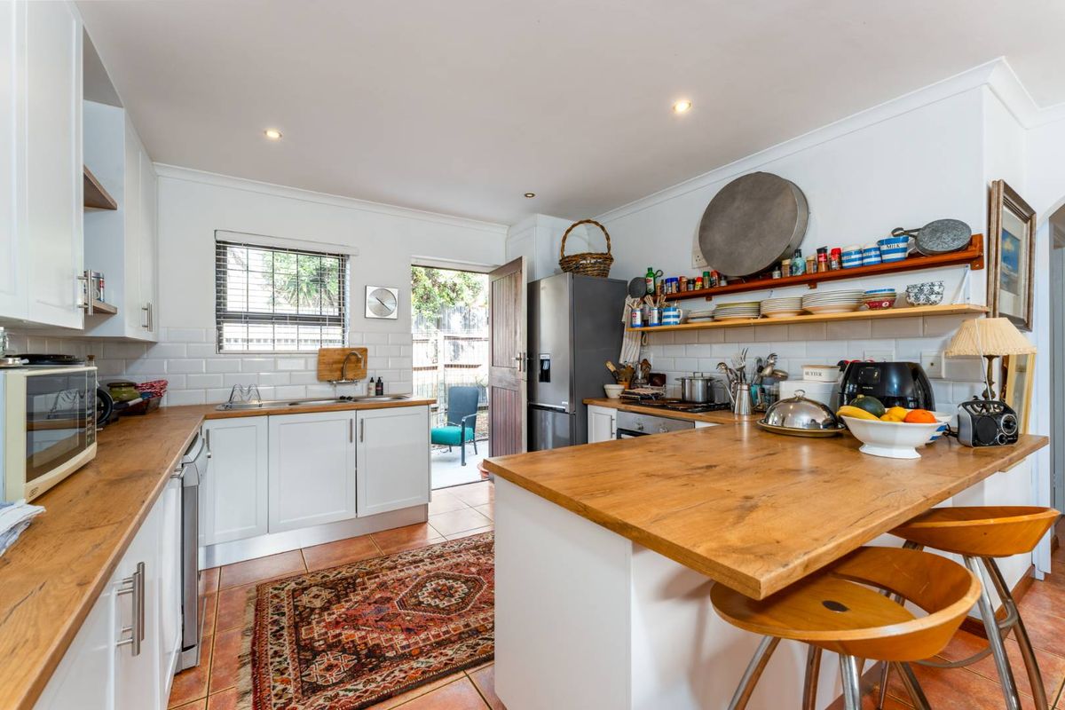 A functional kitchen featuring white cabinetry, wooden countertops, a breakfast bar, subway tile backsplash, and direct access to the rear outdoor area.