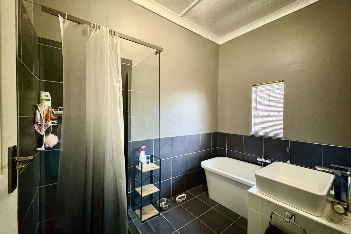 Modern bathroom featuring a freestanding bathtub, a separate glass-enclosed shower, and a contemporary vessel sink vanity with dark floor and wall tiling.