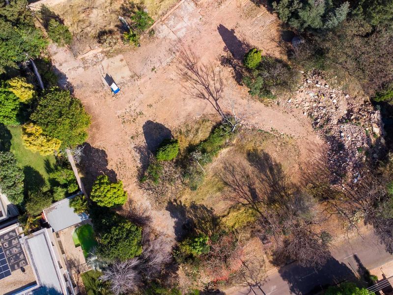 An aerial view of a vacant residential plot featuring mature trees and a cleared building site with some debris present.