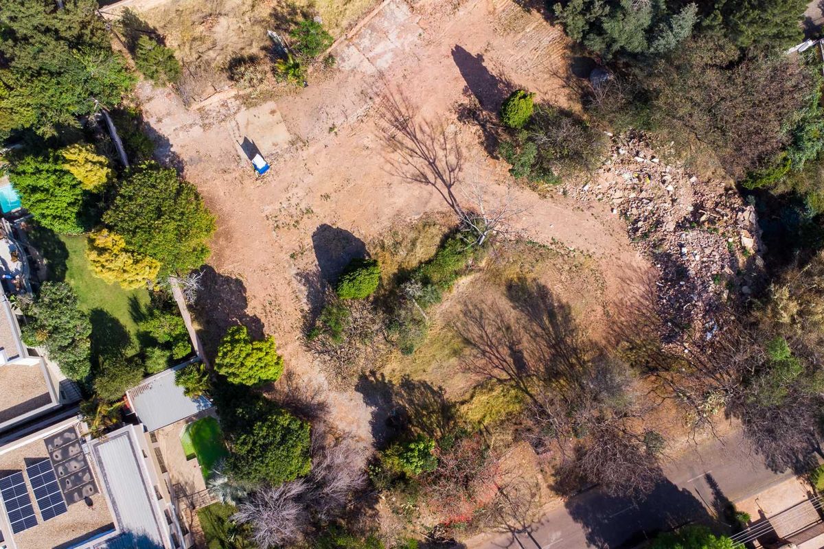 An aerial view of a vacant residential plot featuring mature trees and a cleared building site with some debris present.