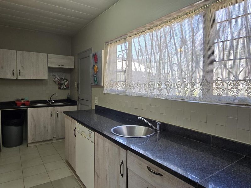 Functional kitchen featuring laminate cabinetry, granite countertops, and a stainless steel sink, with tiled flooring and security bars on the windows.
