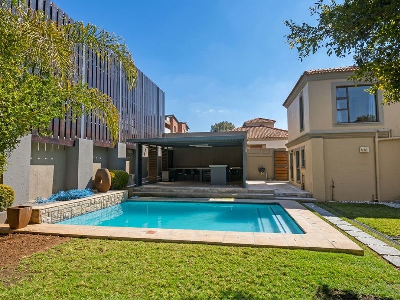 A well-maintained outdoor entertainment area featuring a swimming pool, paved surround, and a covered patio with a built-in bar.