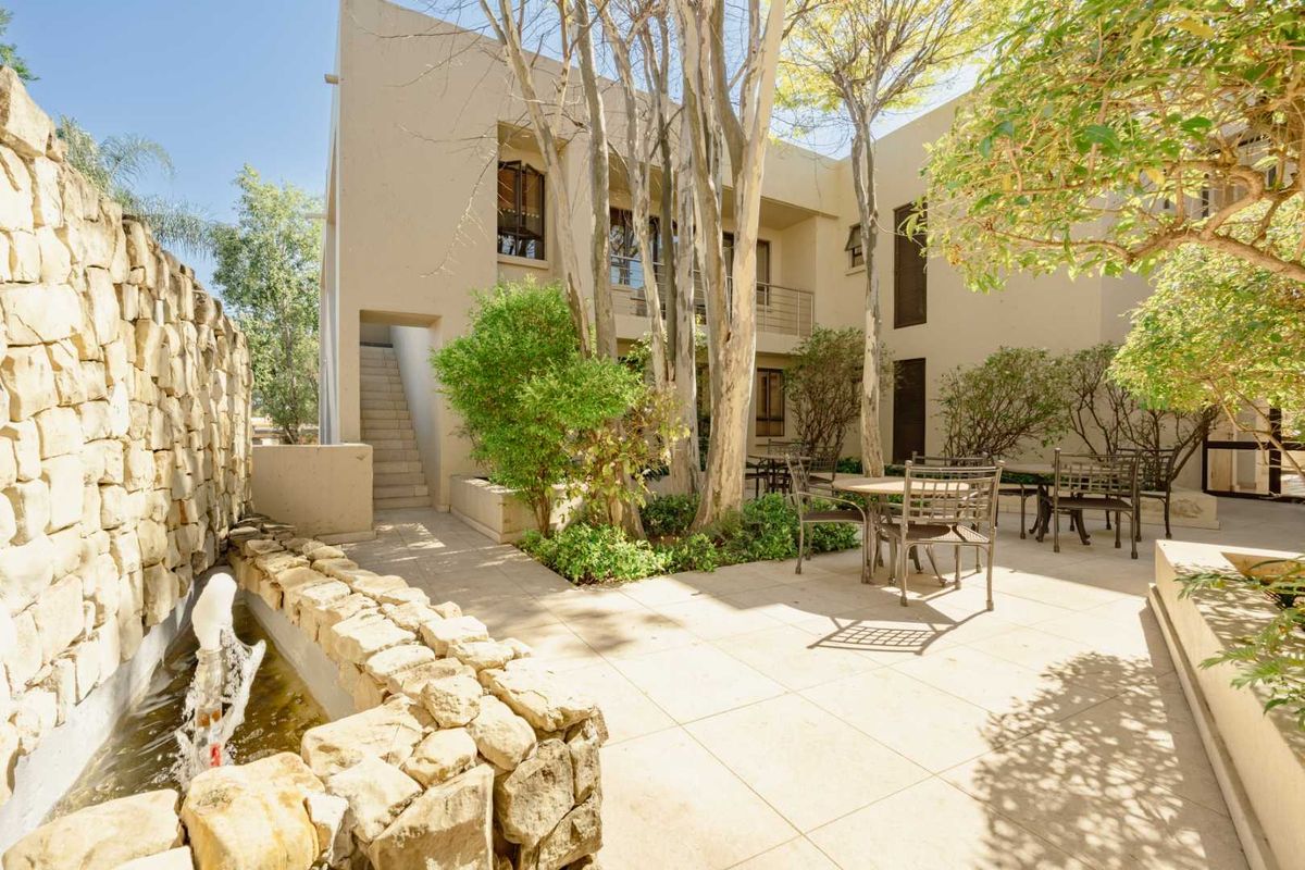 A well-maintained rear courtyard featuring a stone-clad water feature, paved patio area, and access to an external staircase and upper-level balcony.