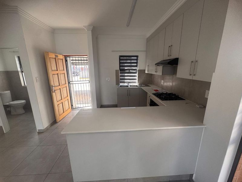 Modern kitchen featuring white built-in cabinetry, stone countertops, gas hob, extractor fan, and tiled flooring, with an adjacent view of the bathroom area.