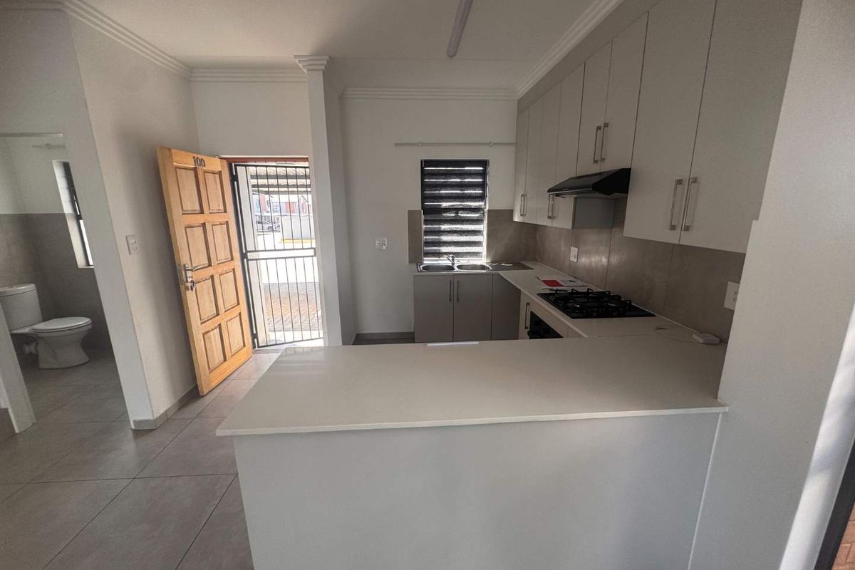 Modern kitchen featuring white built-in cabinetry, stone countertops, gas hob, extractor fan, and tiled flooring, with an adjacent view of the bathroom area.