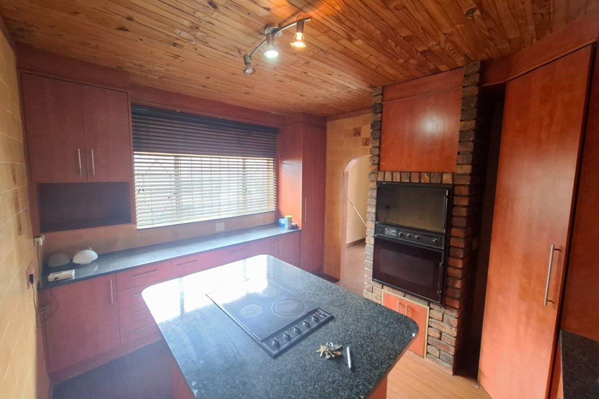 A functional kitchen featuring timber ceilings, granite countertops, a central island with an electric hob, and a built-in oven set into a brick feature wall.